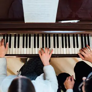Child playing a piano with teacher helping over head shot